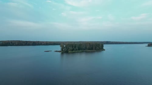 The Camera Flies Low Over the Water Surface of the River Towards a Small Island