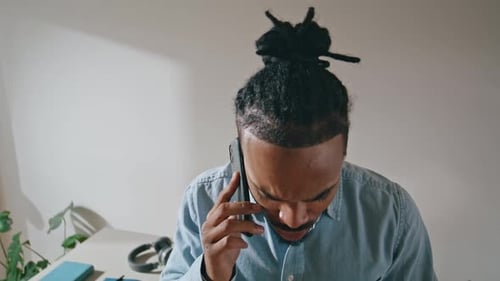 Young man with bun talking on phone indoors