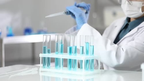 Scientist taking blue liquid from test tube at white table in laboratory, closeup