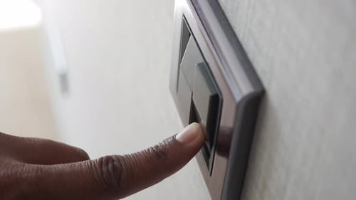 Finger presses light switch on wall panel