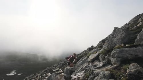 Woman Traveler With Backpack Hiking On Rocky Cliff On A Cloudy Day - slow motion