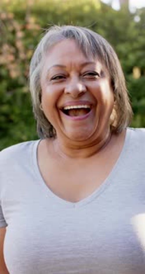 Vertical video: Smiling senior woman enjoying outdoor time in casual attire, feeling happy
