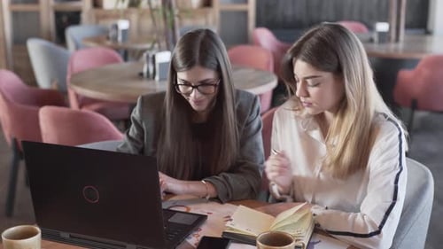 Jóvenes empresarias debaten sobre información y toman notas en un escritorio frente a la cámara