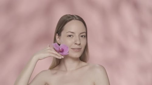 A Woman Touches an Orchid Flower to the Clean Skin of Her Face and Bare Shoulders A Woman with an