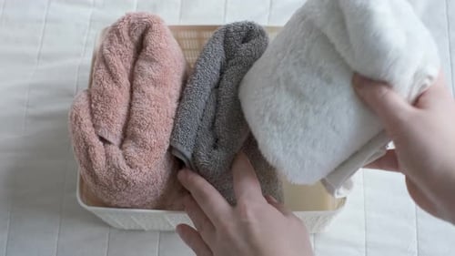Female hands folding towels in plastic box on the background of a white bedspread, top view.