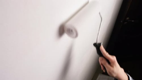 White Paint Roller Moving Vertically Along the Wall Applying a Fresh Layer of Paint Closeup View