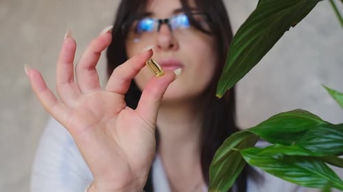 Woman Holding Gold Gel Capsule in Hand