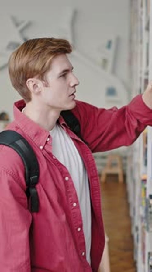 Freshman Student Takes Book with Green Cover From Rack Shelf