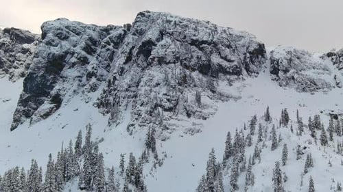 Rocky Cliffs Covered in Snow During Cloudy Winter Day BC Canada Aerial