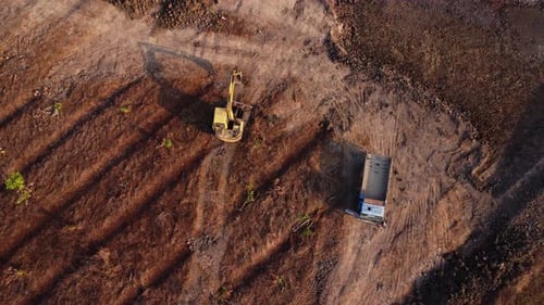 Aerial view of a wheel loader excavator with a backhoe loading sand into a heavy earthmover
