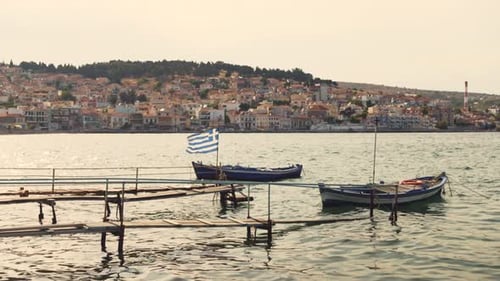 Wooden fishing boats floating by the harbour of Mitylene, with a Greek flag fluttering in the wind a