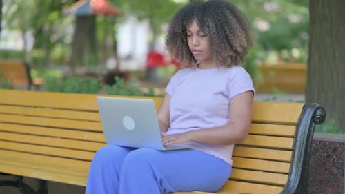 Woman Using Laptop on Park Bench Reacts