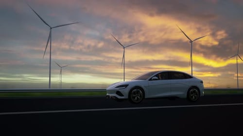 Coche eléctrico que pasa junto a las turbinas eólicas al atardecer
