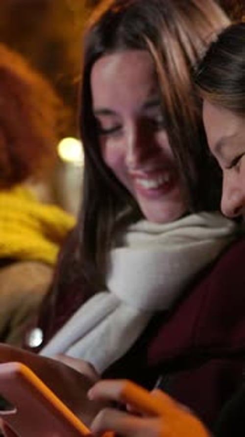 Two Women Looking at Smartphone in City at Night