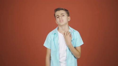 Teen Boy Rubbing Sore Throat on Orange Background