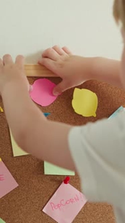 Cute Blond Preschooler Plays with Paper and Cork Board