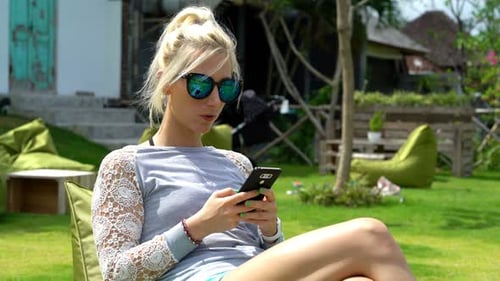 Smiling woman texting on smartphone in sunny garden cafe on summer day