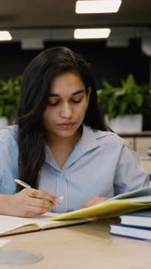 Focused Woman Studying and Writing in Notebook Indoors