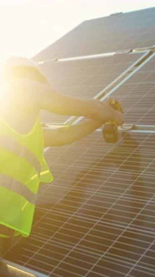 A Worker is Actively Installing Solar Panels Using a Power Tool in a Construction Site