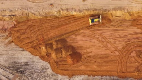 Aerial dolly out shot of Bulldozer leveling dirt in an excavation site with visible tracks