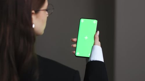 Woman is Holding Smartphone with Green Screen at Home or Office Using Smartphone Watching Green