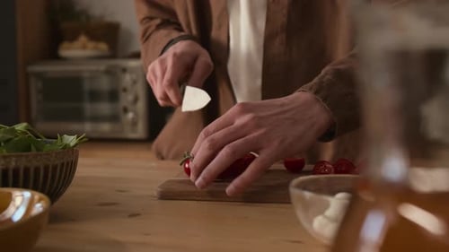 Unrecognizable Man Cutting Cherry Tomato in Half on Wooden Cutting Board