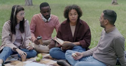 Group of Students Drinking Coffee and Discussing Books Enjoying Picnic in Park on Summer Day