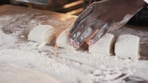 African american male baker working in bakery kitchen, cutting dough on counter in slow motion