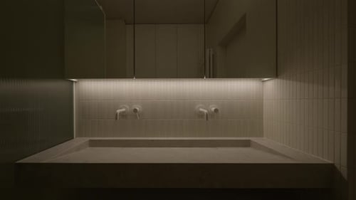 Wide double tiled washbasin with two wall mounted faucets under LED light.