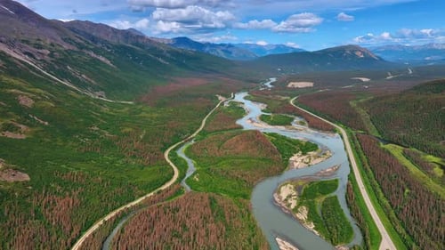 Flying above the delta of the river near the highway. Stunning mountains range in Alaska.