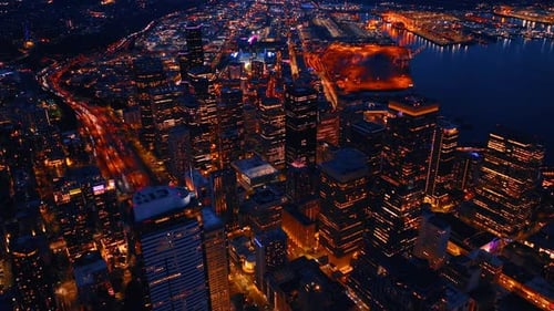 Brightly illuminated cityscape at night. Wide multi-lane highway is packed with cars.