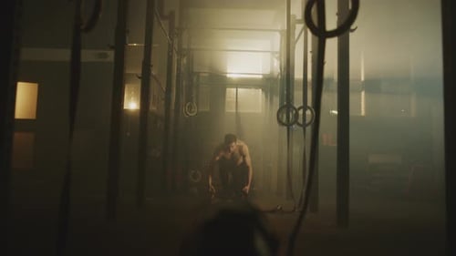 Muscular Man Exercising with Battle Ropes in Dark Gym