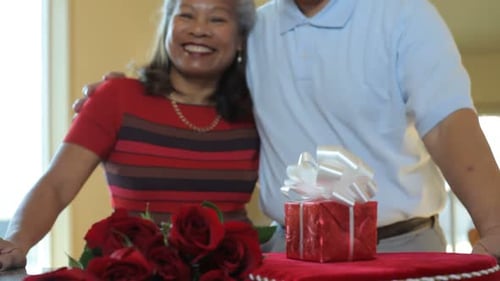 Smiling couple celebrates anniversary with roses and gift