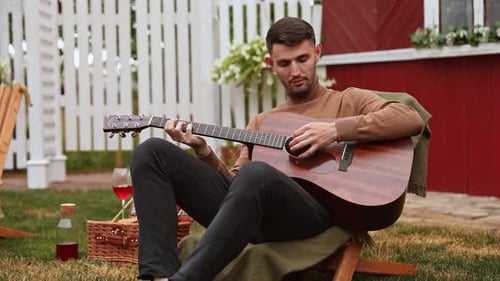 Young Man Plays Guitar Outdoors on Lawn