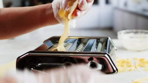 Frau benutzt Nudelmaschine, um frischen Nudelteig in der Küche zuzubereiten und kocht in einem italienischen Restaurant