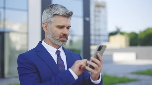 Mature Man Using Smartphone Outside Office Building