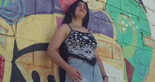 A young girl wearing urban street fashion is in the city, with graffiti in the background.
