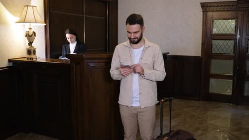 Young Man Using Smartphone in Hotel Lobby Near Reception Desk
