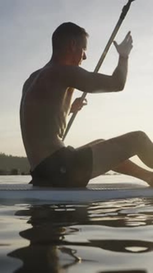 Man Paddle Boarding on Water at Sunset