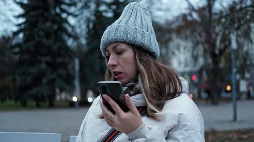 Portrait of Mature Woman in Wool Hat Standing on the Urban Street with Mobile Phone in Hand