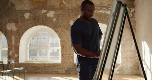 Closeup Shooting A Black Male Doctor in a Blue Uniform Writes Explanations on a Canvas with a Green