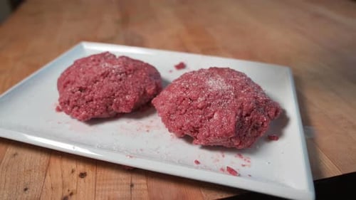 Une main met du sel sur des galettes de burger végétaliennes Impossible, angle élevé, gros plan