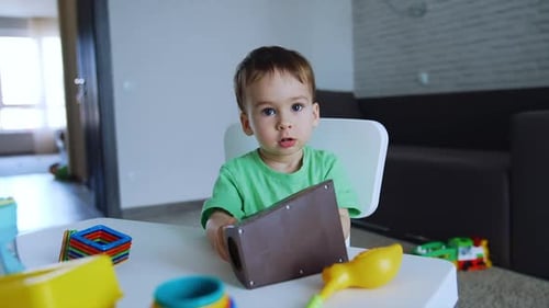 Sweet Caucasian boy plays with toys sitting at the desk. Lovely toddler in his playroom.