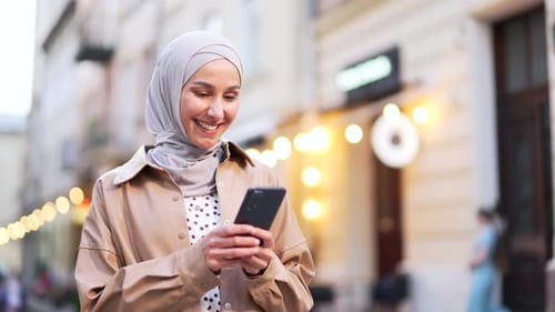 Attractive young muslim woman in hijab standing on city street using smartphone mobile phone Outdoor