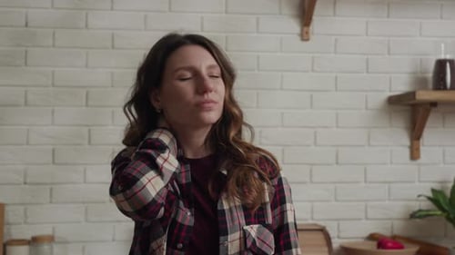 Une femme se détend dans la cuisine, soulageant visiblement les douleurs au cou avec une expression calme et sereine