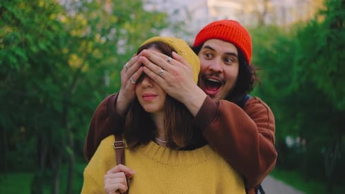 A Playful Moment in the Park As a Man Surprises His Girlfriend By Covering Her Eyes After a Joyful