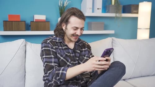 Smiling Man Using Phone on White Couch Indoors