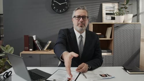 Empresário de meia idade estendendo a mão com um sorriso esperando um aperto de mão no escritório