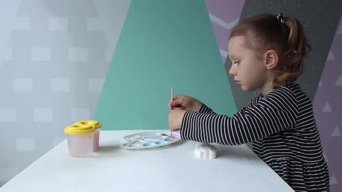 Young Girl Painting with Brush at Table Indoors