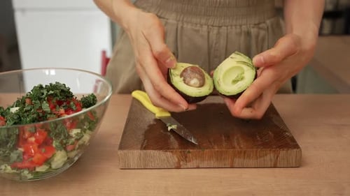 Woman cutting avocado for salad at home